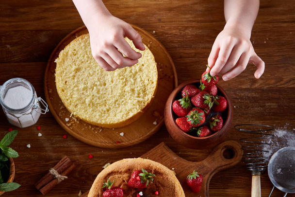 Close up of girls hands adding cream on top of delicious strawberry cake, close up, selective focus. - Valokuva, kuva