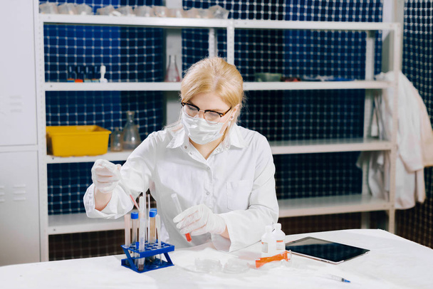 μια εστιασμένη φοιτητής-επιστήμη λειτουργεί σε ένα εργαστήριο με έναν σωλήνα δοκιμής. Η κοπέλα επιλέγει το σωστό δοκιμαστικό σωλήνα - Φωτογραφία, εικόνα