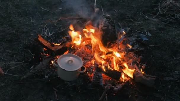 A comida cozinha-se na fogueira em uma panela. As mãos das mulheres tocam com o pote
. - Filmagem, Vídeo