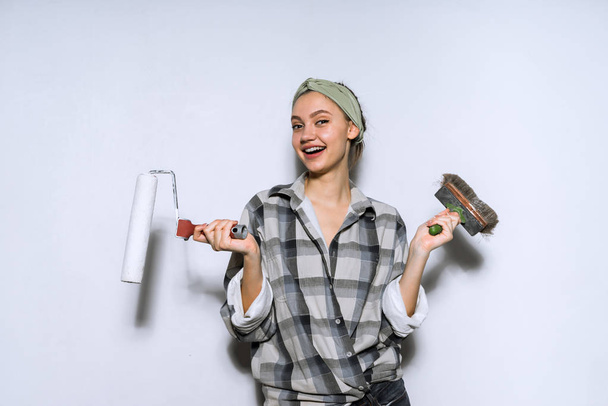 happy smiling young girl paints the walls with a roller and brush in white - 写真・画像