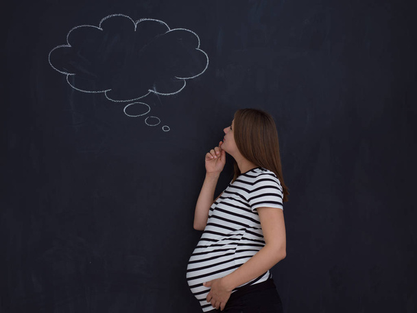 young pregnant woman thinking about names for her unborn baby to writing them on a black chalkboard - Foto, immagini