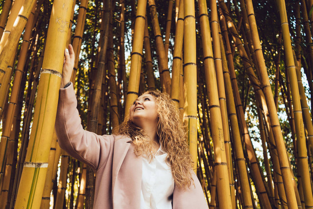 joyful happy curly woman admiring the tall bamboo trees in the park in the spring - Zdjęcie, obraz