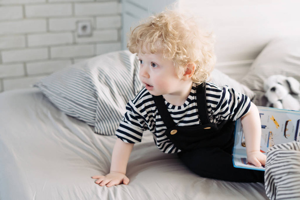 cute blonde baby boy in cute clothes sitting on the bed and smiling - Foto, Imagem