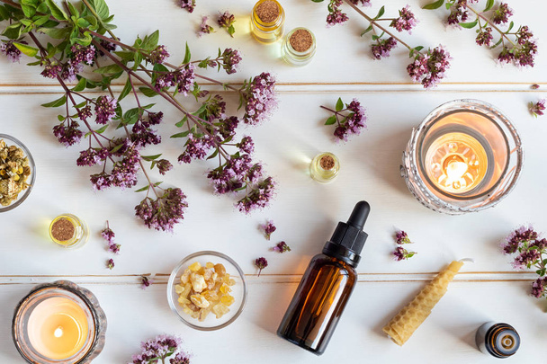 Bottles of essential oil with fresh blooming oregano twigs, frankincense resin and other herbs - Foto, Imagem