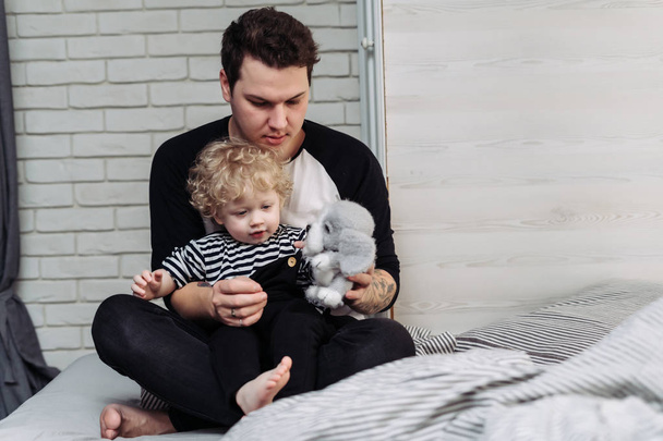 a young kind dad holding his little curly-haired son in his arms, playing with toys and spending time together - Zdjęcie, obraz