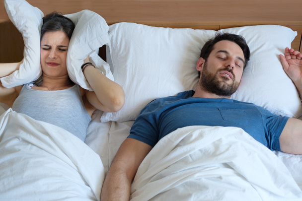 Stressed woman covering ears with a pillow as she is annoyed by the snoring of her boyfriend - Photo, Image