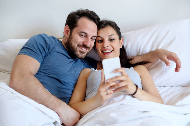 Couple in love in the bed holding smartphone - Zdjęcie, obraz