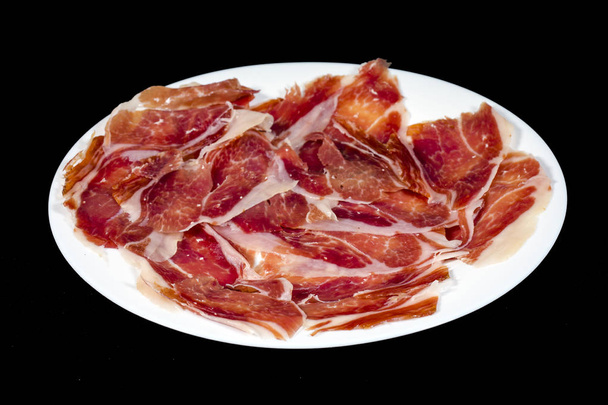 Serrano ham, ham, typical and delicious Spanish food, Isolated background in black. Selective focus foreground - Photo, Image