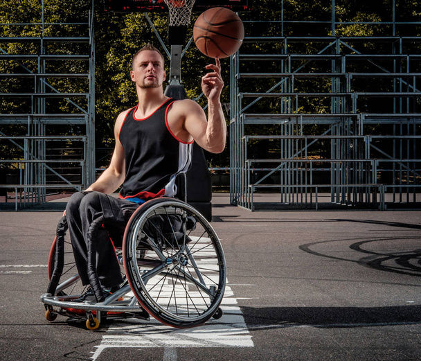 Giocatore di pallacanestro disabile in sedia a rotelle che gira pallacanestro sul suo dito sul terreno di gioco aperto
. - Foto, immagini