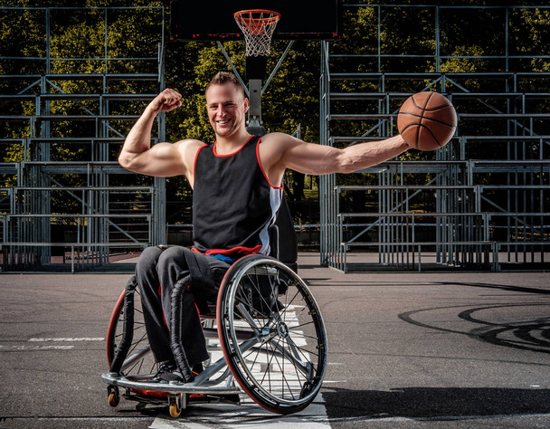 Ευτυχισμένος μπασκετμπολίστας σε μια αναπηρική καρέκλα πόζα με μια μπάλα ανοιχτή gaming επιτόπου. - Φωτογραφία, εικόνα