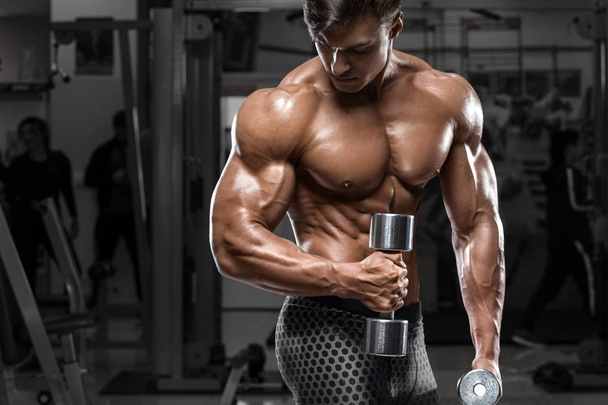 Hombre muscular sexy en el gimnasio haciendo ejercicio para bíceps. Fuertes abdominales masculinos desnudos del torso, haciendo ejercicio
 - Foto, imagen