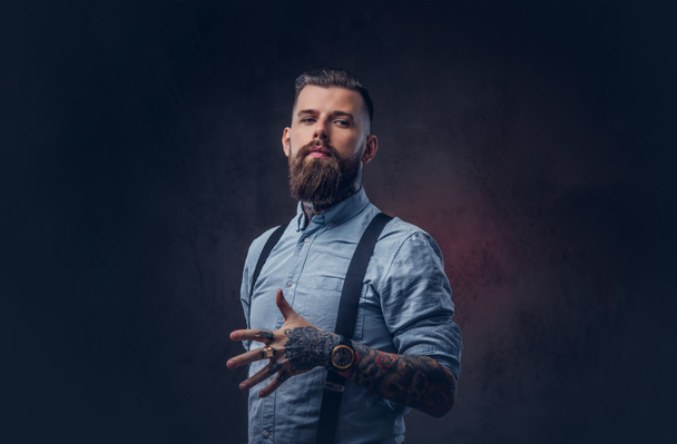 Portrait of a handsome old-fashioned hipster in a blue shirt and suspenders. Isolated on a dark background. - Foto, imagen