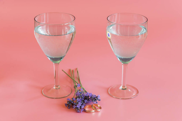 Wedding rings with glasses of wine and lavender flowers on a pink background. - Fotoğraf, Görsel