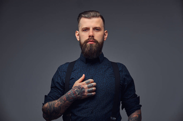 Πορτρέτο του ένα σοβαρό όμορφος ντεμοντέ hipster στο πουκάμισο και τιράντες. Απομονωμένα σε σκούρο φόντο. - Φωτογραφία, εικόνα