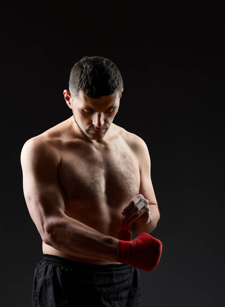 Low key studio portrait of handsome muscular fighter practicing boxing on dark blurred background - Photo, Image