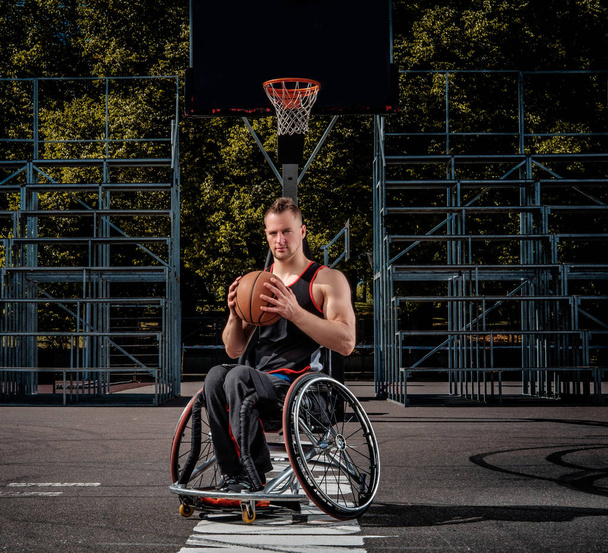 Калека баскетболист в инвалидной коляске держит мяч на открытой игровой площадке
. - Фото, изображение
