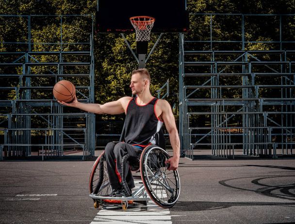 Fuerte jugador de baloncesto en silla de ruedas posar con una pelota en campo de juego abierto
. - Foto, imagen