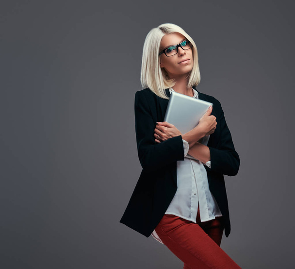 Femme blogueuse à la mode intelligente dans des vêtements et des lunettes modernes, pose avec tablette numérique. Isolé sur un fond gris
. - Photo, image