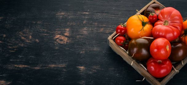 Valikoima tomaatteja puulaatikossa. Tuoreita vihanneksia. Musta puinen tausta. Huippunäkymä. Kopioi tila
. - Valokuva, kuva