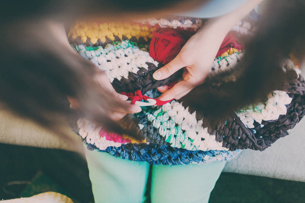 女性は、太い糸から編み編み物です。古着から糸します。自家製のスレッドの敷物。女性の手は、フックを保持します。ヴィンテージ カーペット。ニットの格子縞。手作り。家の趣味. - 写真・画像