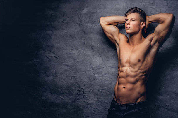 Beautiful shirtless young man model with nice muscular body posing at a studio. Isolated on a dark background. - Photo, Image