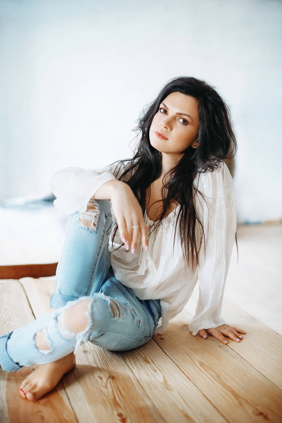 Hermosa joven posando en blusa blanca y jeans en estudio
  - Foto, Imagen