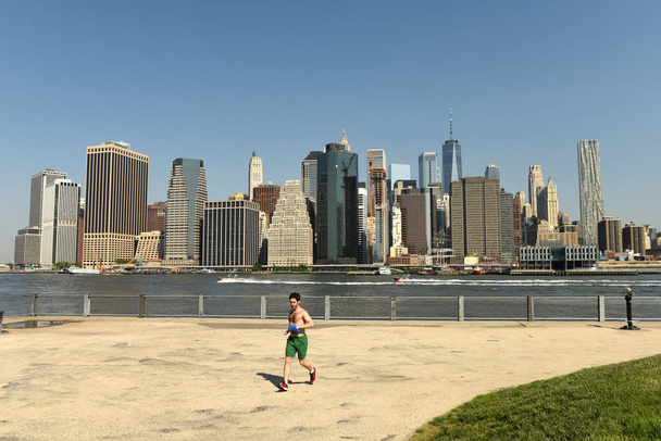 New York, USA - May 25, 2018: A man on run in Brooklyn Bridge Park with financial district in lower Manhattan at the background. - Photo, image