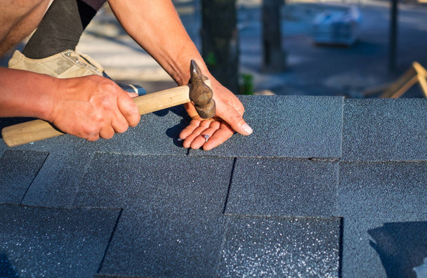 Worker repair corner bitumen roof shingles with hammer and nails. - Foto, Bild
