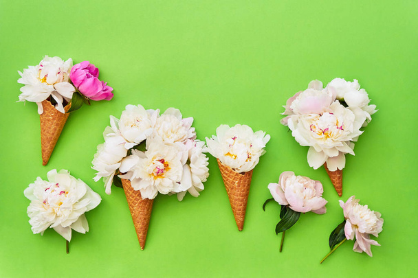 Waffle ice cream cones with white peony flowers on green background. Summer concept. Copy space, top view.  - Photo, Image