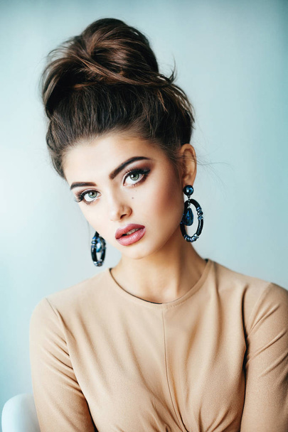 Beautiful young woman posing in fashion beige top and beautiful earrings  in studio  - Zdjęcie, obraz