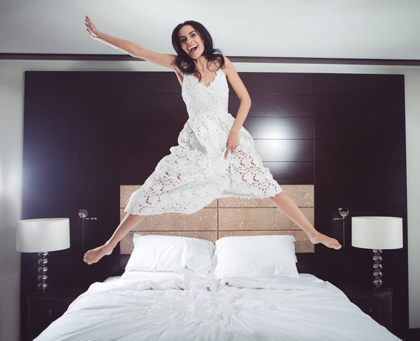 Cheerful young woman jumping in bedroom - Photo, image