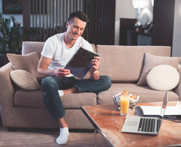 Feliz jovem está lendo revista na sala de estar
  - Foto, Imagem