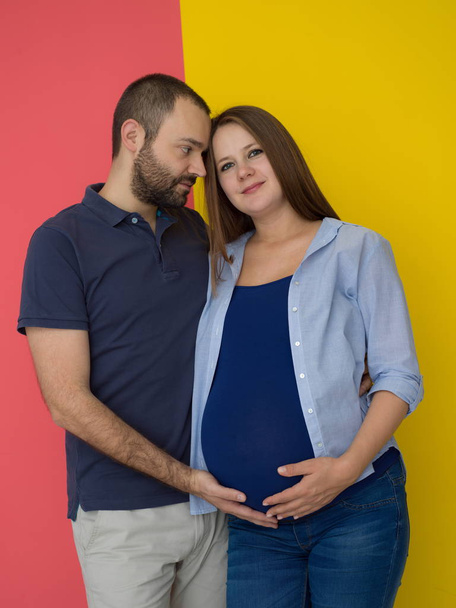 Портрет счастливой молодой пары, мужчина держит беременную жену живота изолированы на красочном фоне
 - Фото, изображение