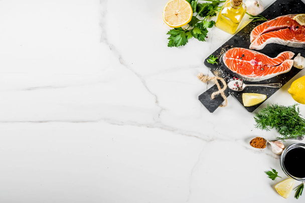 Νωπό σολομό ψάρια μπριζόλες με λεμόνι, βότανα, ελαιόλαδο, έτοιμη για τη σχάρα, πλάκα κοπής, φόντο λευκό μαρμάρινο αντίγραφο χώρο από πάνω - Φωτογραφία, εικόνα