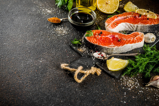 rohe Lachsfischsteaks mit Zitrone, Kräutern, Olivenöl, grillfertig, Schieferschneidebrett, dunkel rostiger Hintergrund Kopierraum - Foto, Bild
