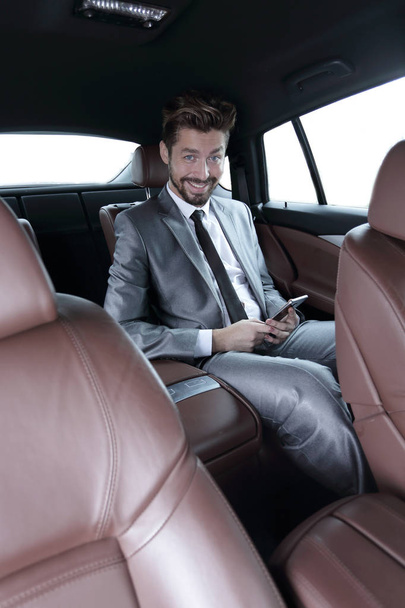 man in suit sitting in car and reading messages on smartphone - Foto, immagini