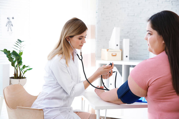Female doctor measuring blood pressure of overweight woman in clinic - Fotó, kép