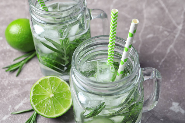 Natural lemonade with cucumber, lime and rosemary in mason jars on table, closeup - Фото, изображение