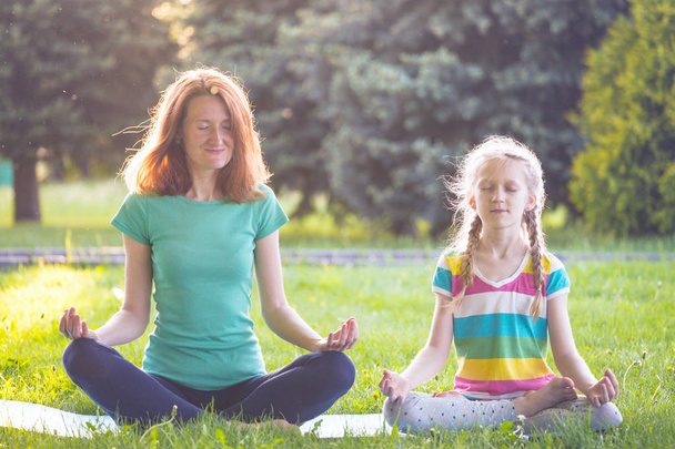 Healthy lifestyle - mom and daughter doing yoga in the park. Healthy and Yoga Concep - Фото, зображення