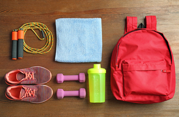 Flat lay composition with sports bag and gym equipment on wooden floor, top view - Foto, afbeelding