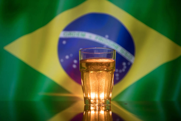 Creative concept. Pint of fresh beer on table with blurred flag of Brazil on background or Glass of lager beer ready for drink. Copy space. Selective focus - Foto, immagini