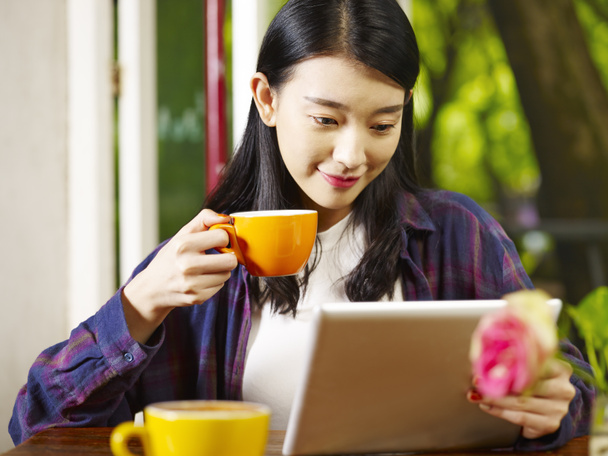 beautiful young asian woman using digital tablet while drinking cappuccino in coffee shop. - Photo, Image
