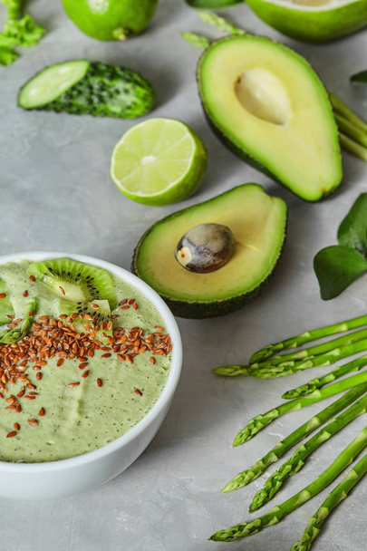 bowl with green smoothie made of cucumber, avocado, asparagus, lime and flax seeds on concrete background - Photo, image