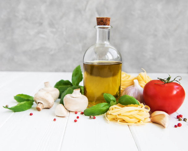 Italialaiset elintarvikkeiden ainesosat, oliiviöljy, mausteet, pasta ja tomaatit valkoisella puupöydällä
 - Valokuva, kuva