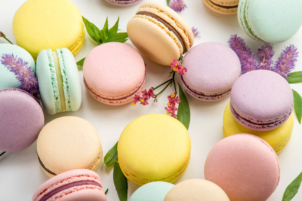 bunte Macarons mit Blättern und roten Blüten auf weißem Hintergrund. Französisch zartes Dessert. schöne Komposition - Foto, Bild