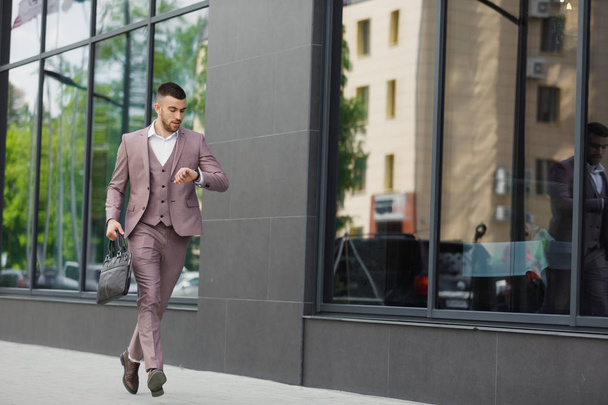 Young businessman with a briefcase running in a city street on a background of wall - Photo, image