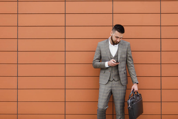 бізнесмен в костюмі і використовує сучасний смартфон біля офісу рано вранці, успішний роботодавець, щоб укласти угоду, стоячи біля хмарочоса
 - Фото, зображення