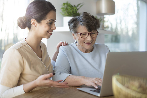 Счастливый ассистент учит пожилую женщину искать в Интернете на ноутбуке
 - Фото, изображение