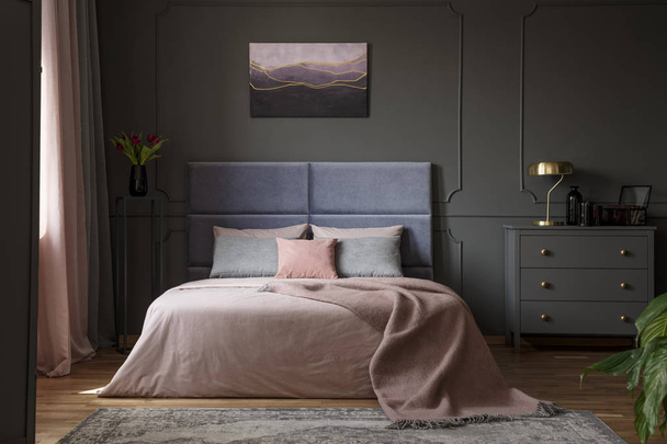 Gold lamp on grey cabinet next to bed in pastel bedroom interior with violet painting - Fotoğraf, Görsel