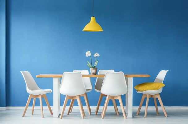 Blue dining room interior with a big table, white chairs and yellow chandelier - Foto, Bild
